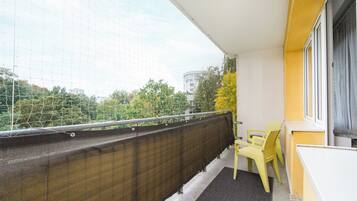 Un balcone con un muro giallo, una ringhiera in rete nera e due sedie gialle.