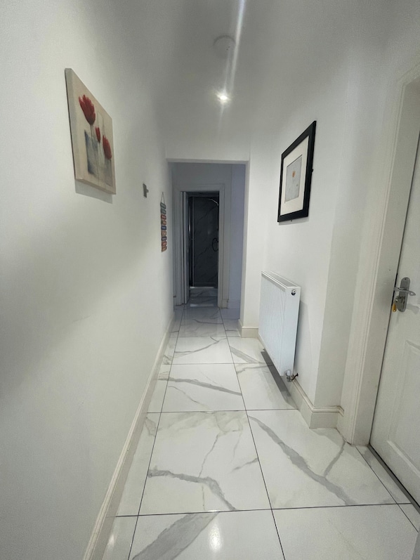 Un corridoio con pareti bianche, pavimento in marmo, un quadro incorniciato e un termosifone.