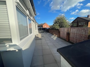 Un cortile residenziale con patio in pietra, recinzione in legno e cielo sereno.