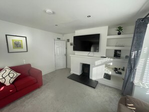 A living room with a red sofa, a flat-screen TV mounted above a fireplace, and a white door with an exit sign.