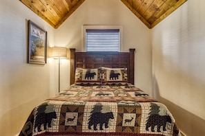 A bedroom with a wooden ceiling, a window with blinds, a bed with a quilted headboard, and a bedside lamp. - Close to Pkwy~Htd Pool~View~Hot Tub~Arcade~Fam Fav (Sevierville)
