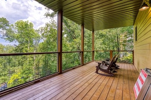 A wooden deck with a view of a forest, a bench, and a covered area with a metal roof. - Close to Pkwy~Htd Pool~View~Hot Tub~Arcade~Fam Fav (Sevierville)