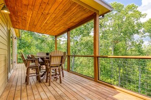 A wooden deck with a table and chairs, surrounded by a metal railing, overlooking a forested area. - Close to Pkwy~Htd Pool~View~Hot Tub~Arcade~Fam Fav (Sevierville)