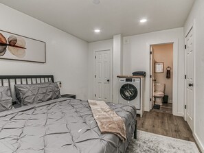Een slaapkamer met een bed, een wasmachine en een toilet in de aangrenzende ruimte.