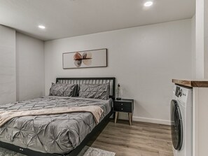 Ein Schlafzimmer mit einem Bett, einem Nachttisch, einer Waschmaschine und einem Wandbild.