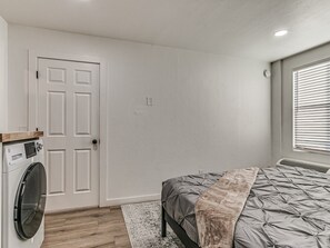 A bedroom with a bed, a washing machine, a door, and a window with blinds. - Remodeled Downtown 1Bed  #8 (Oklahoma City)