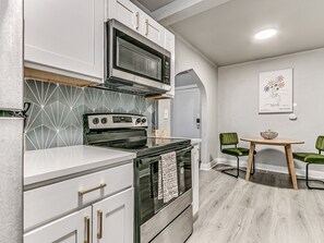 A modern kitchen with white cabinetry, a built-in microwave, and a stove. There is a wooden table with chairs in the dining area. - Stylish Midtown OKC Condo (Oklahoma City)