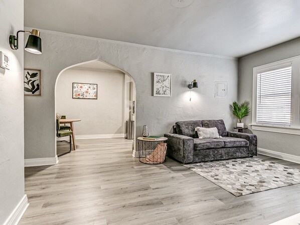 Ein modernes Wohnzimmer mit einem grauen Sofa, einem gemusterten Teppich und einem Essbereich mit einem grünen Stuhl und Tisch.