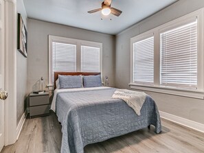 A bedroom with a bed, nightstands, a ceiling fan, and windows with blinds. - Stylish Midtown OKC Condo (Oklahoma City)