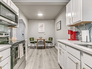 A kitchen with white cabinets, a microwave, a coffee maker, and a dining table with chairs. - Stylish Midtown OKC Condo (Oklahoma City)