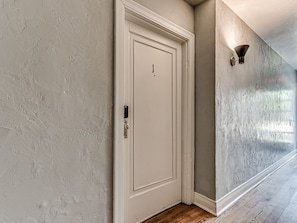 En gang med strukturerede vægge, en hvid dør med lås og en lampe på væggen.