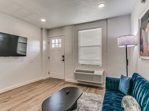 A modern living room with a flat-screen TV mounted on the wall, a blue sofa, a small coffee table, and a standing lamp. - Remodeled 1Bed Apartment #10 (Oklahoma City)