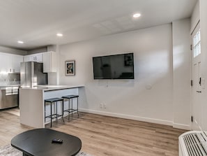 A modern kitchen with a built-in island, bar stools, and a flat-screen TV mounted on the wall. - Remodeled 1Bed Apartment #10 (Oklahoma City)