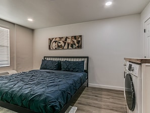 A bedroom with a bed, a washing machine, and a wall-mounted artwork. - Remodeled 1Bed Apartment #10 (Oklahoma City)