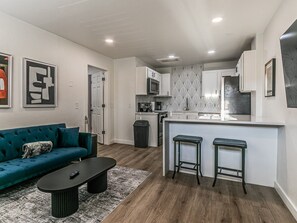 A compact living space with a sofa, a coffee table, a kitchen area with a microwave, and a small bar counter with stools. - Remodeled 1Bed Apartment #10 (Oklahoma City)