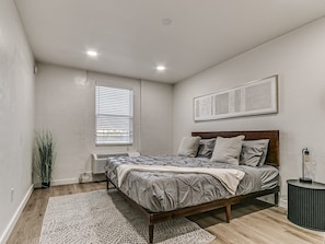 A bedroom with a bed, a bedside table, a floor lamp, and a window with blinds. - Remodeled Urban Apartment 1 BR #1 (Oklahoma City)