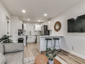 A modern kitchen with white cabinets, a built-in oven, and a large island with bar stools. - Remodeled Urban Apartment 1 BR #1 (Oklahoma City)