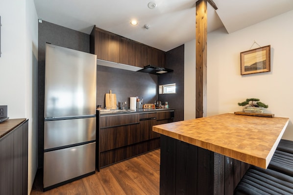 A modern kitchen with a stainless steel refrigerator, wooden cabinets, and a wooden dining table. - Maru  (Shimotakai-gun)