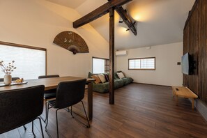A spacious room with a wooden floor, a dining table with chairs, a sofa, and a television mounted on the wall. - Maru  (Shimotakai-gun)