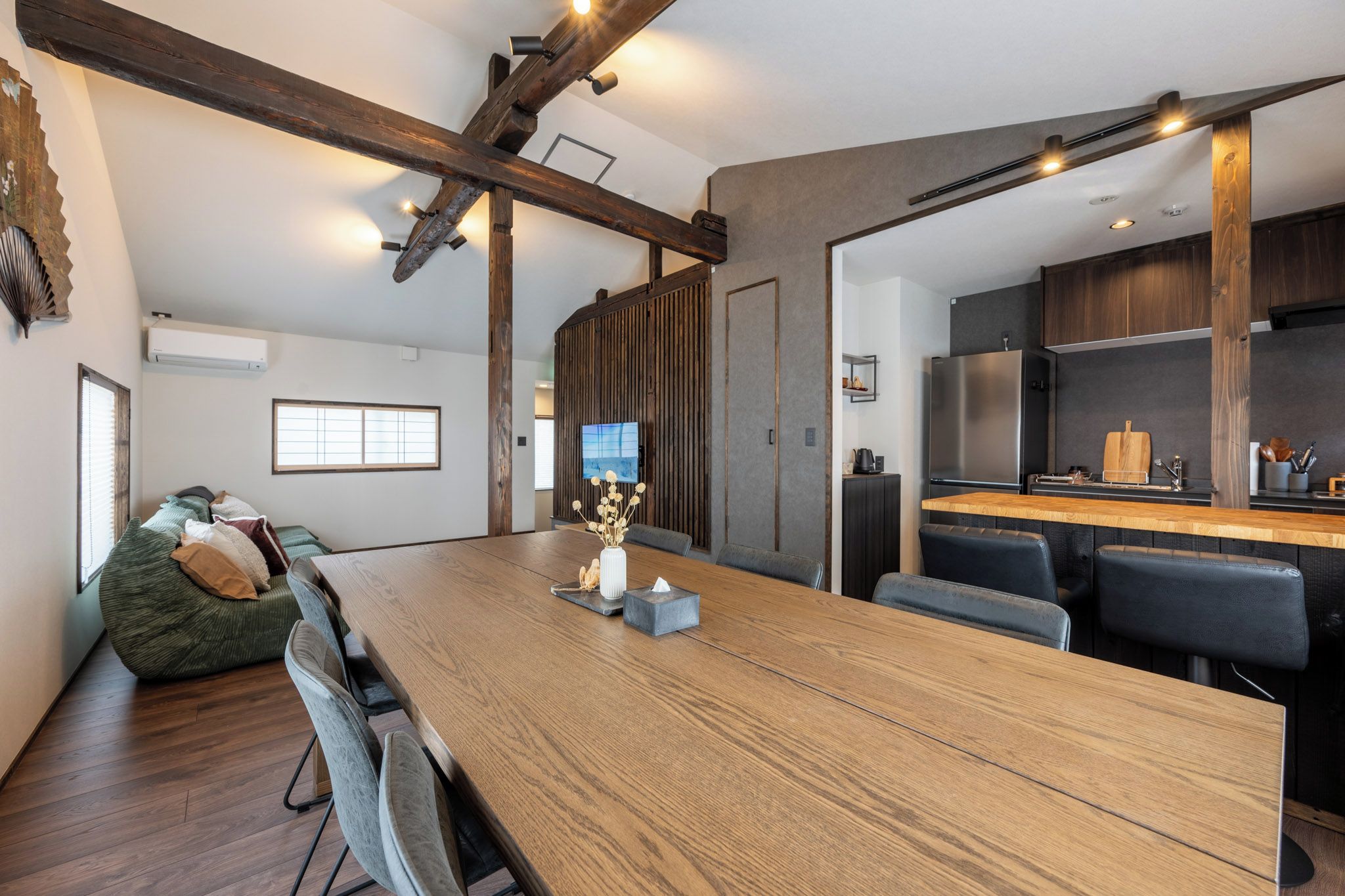 Cozinha moderna com bancada de madeira, eletrodomésticos de aço inoxidável e área de estar com mesa e cadeiras de madeira.