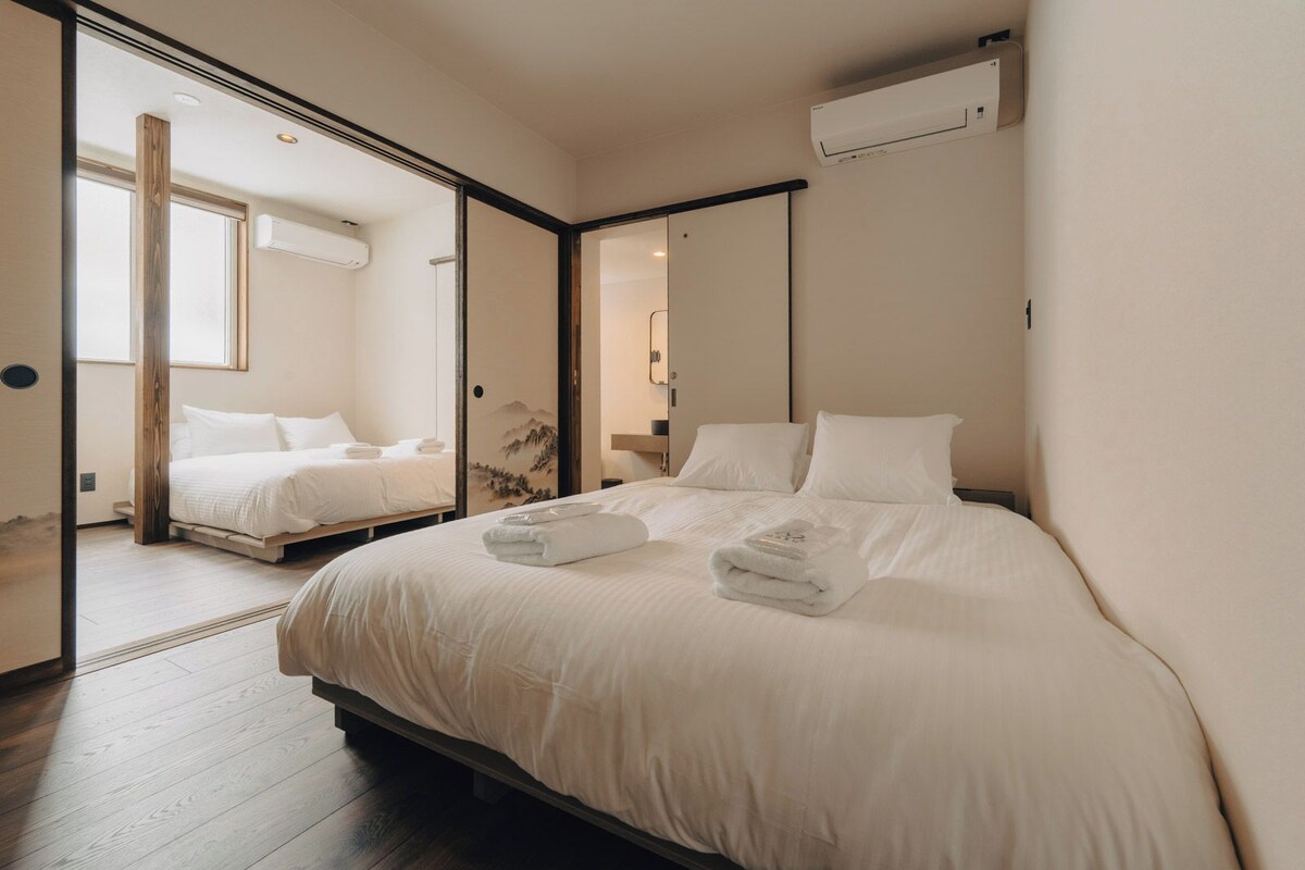 A hotel room with a large bed, a smaller bed, and a sliding door leading to another room.
