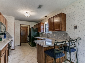 A kitchen with wooden cabinets, a tiled backsplash, and a central island with seating. - Modern OKC Home Near Lake Hefner (Oklahoma City)