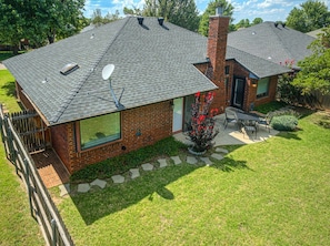 A two-story house with a brick exterior, a satellite dish, and a small patio with a table and chairs. - Modern OKC Home Near Lake Hefner (Oklahoma City)
