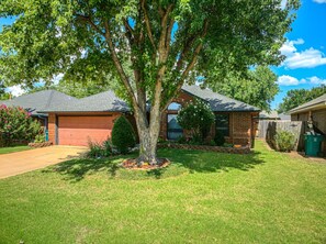 A residential property with a large tree in the front yard, a brick garage, and a wooden fence. - Modern OKC Home Near Lake Hefner (Oklahoma City)