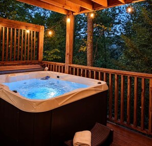 A hot tub on an outdoor deck with wooden railings and string lights. - Cozy Cabin: Private Hot Tub, Fireplace & Mtn Views (Sevier County)