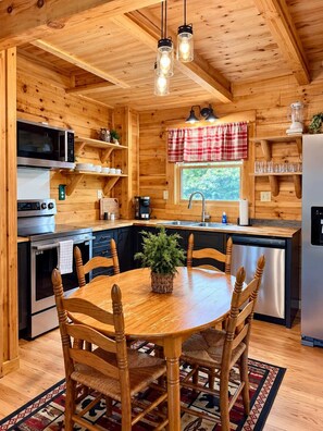 Interior d'una cabana de fusta amb cuina, taula de menjador, cadires i una finestra.