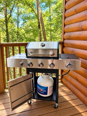 A portable gas grill with four burners, a side shelf, and a propane tank underneath. - Cozy Cabin: Private Hot Tub, Fireplace & Mtn Views (Sevier County)