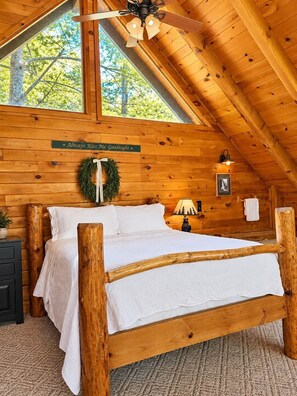 A wooden cabin bedroom with a bed, a ceiling fan, a window, and a sign on the wall. - Cozy Cabin: Private Hot Tub, Fireplace & Mtn Views (Sevier County)
