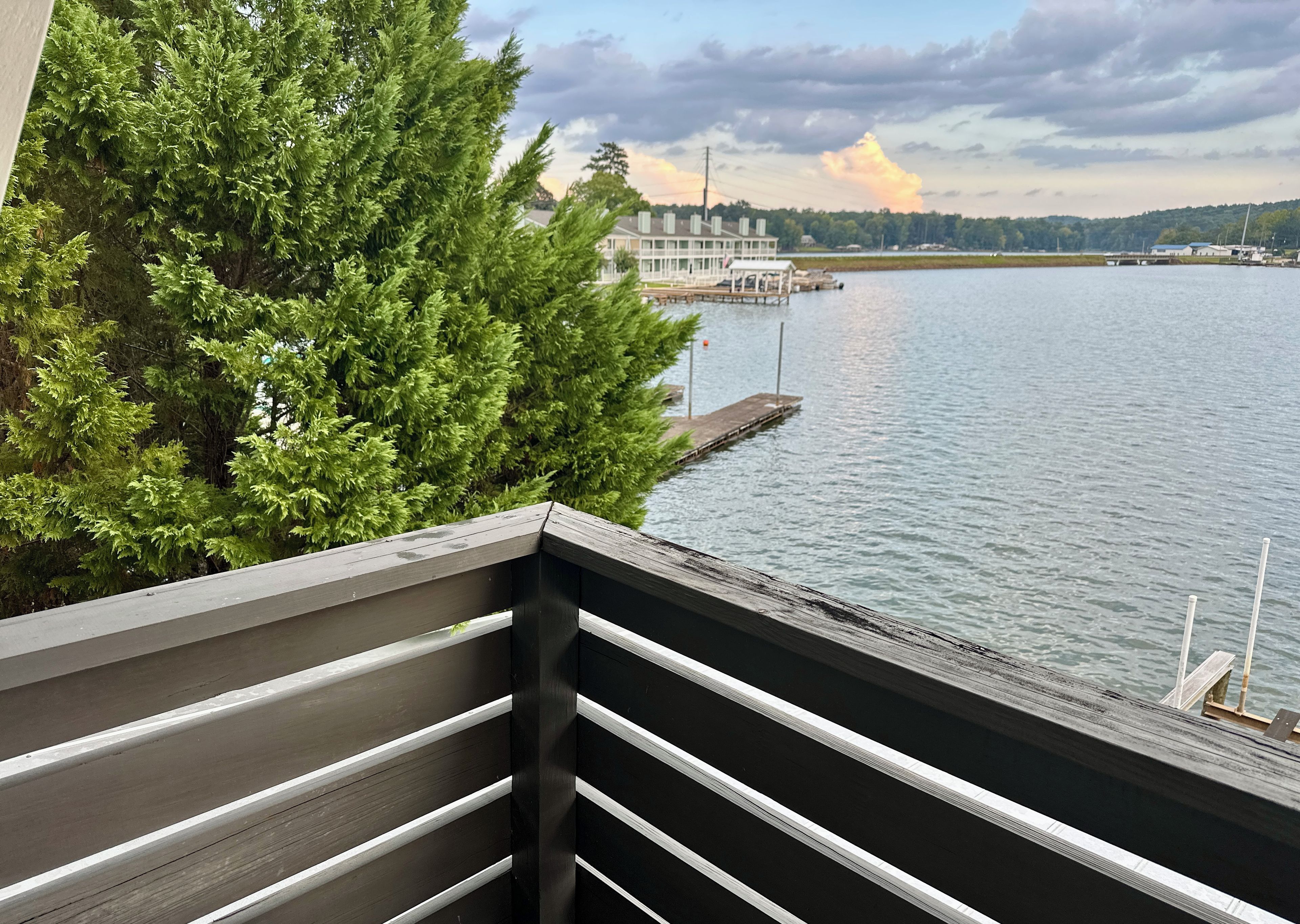 A balcony with a view of a lake, dock, and a building across the water.