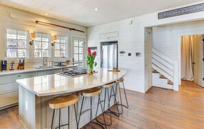 Une cuisine dotée d’un grand îlot central, de tabourets de bar, d’un réfrigérateur en acier inoxydable et d’un plancher en bois.