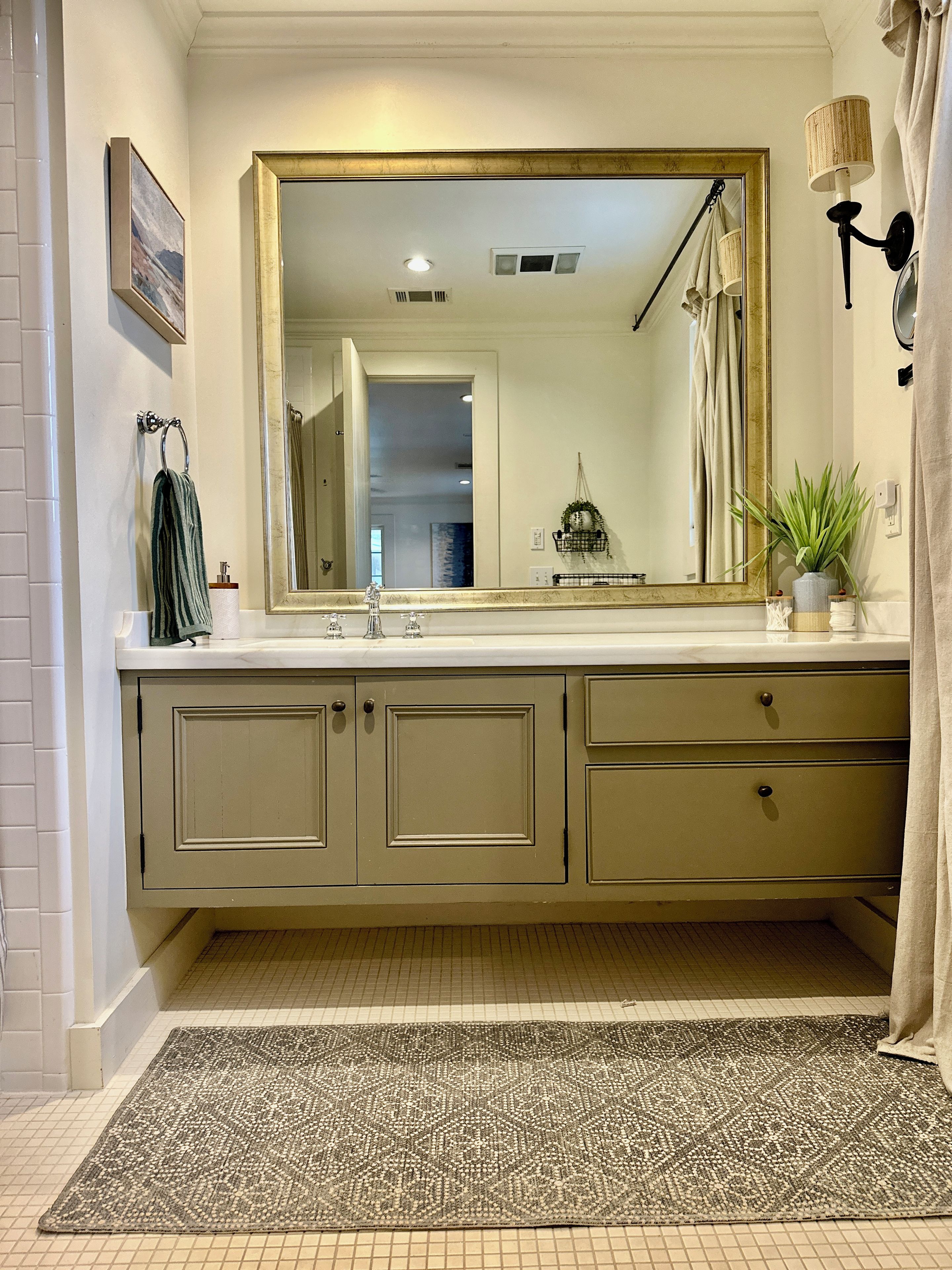 A bathroom with a large mirror, a sink, cabinets, a towel rack, a potted plant, and a shower curtain.