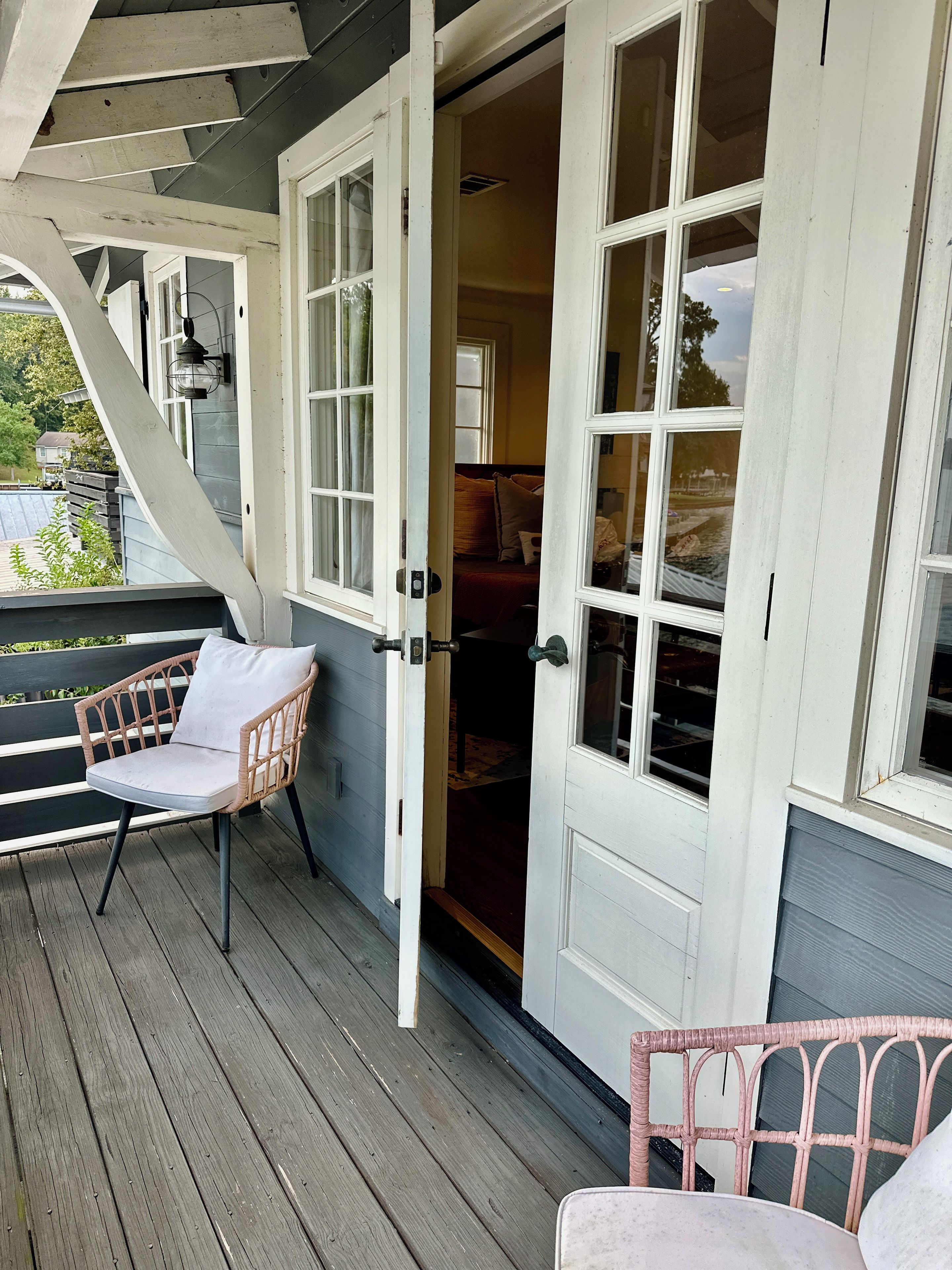 A wooden deck with a wicker chair and a door leading to a room with a bed.