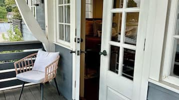 A wooden deck with a wicker chair and a door leading to a room with a bed.