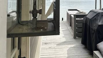 A deck with a view of a body of water, a covered seating area, and a window with a view of the landscape.