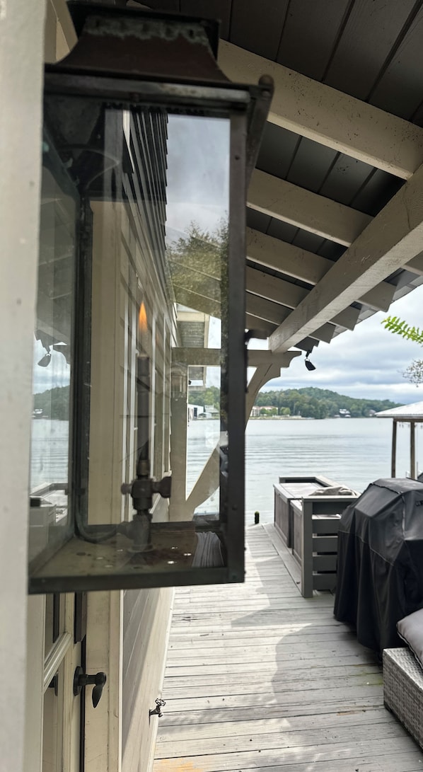 A deck with a view of a body of water, a covered seating area, and a window with a view of the landscape.