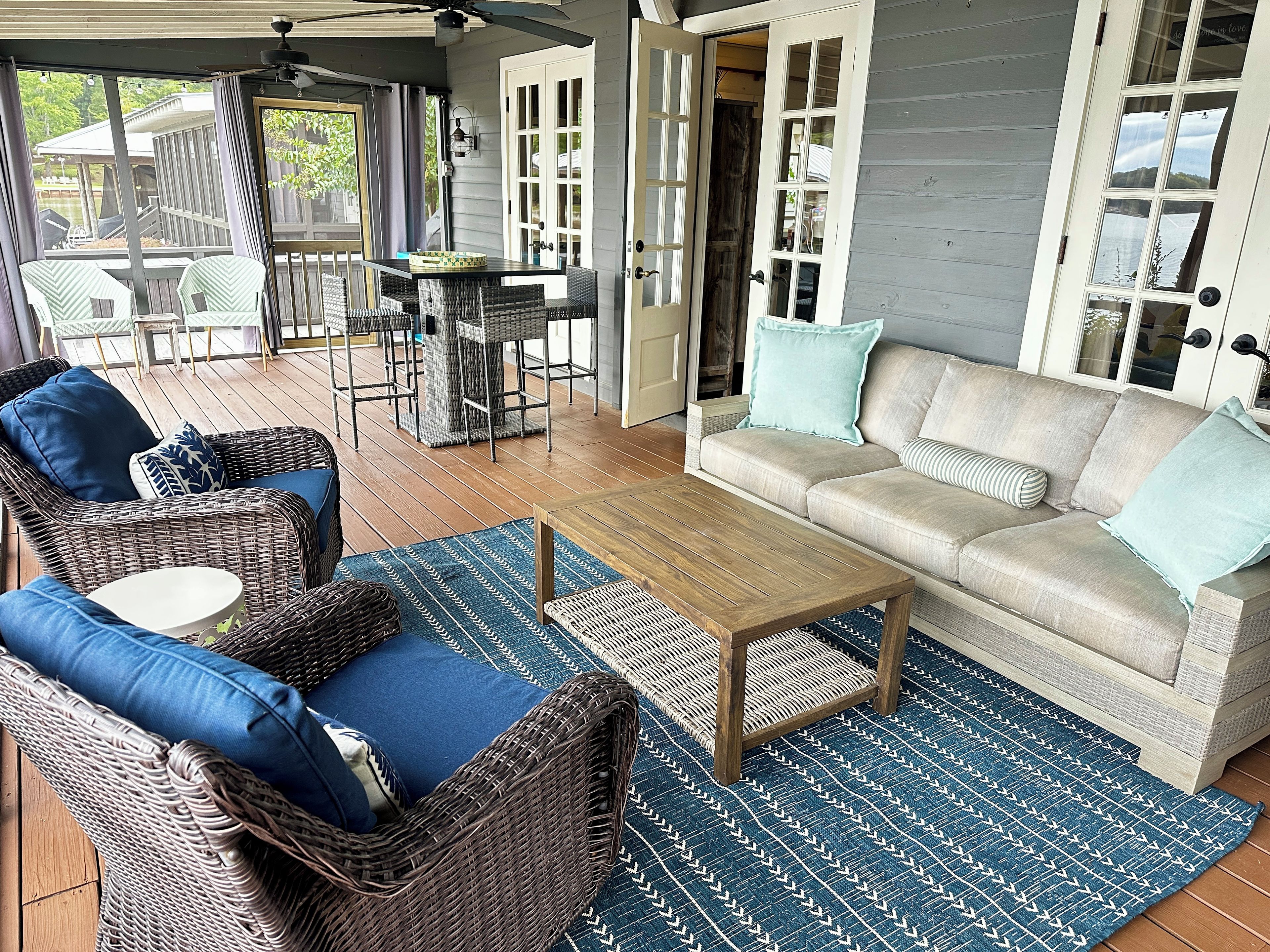 A covered outdoor seating area with wicker furniture, a wooden coffee table, and a patterned rug.