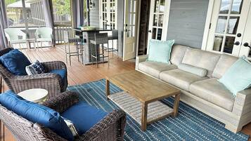 A covered outdoor seating area with wicker furniture, a wooden coffee table, and a patterned rug.