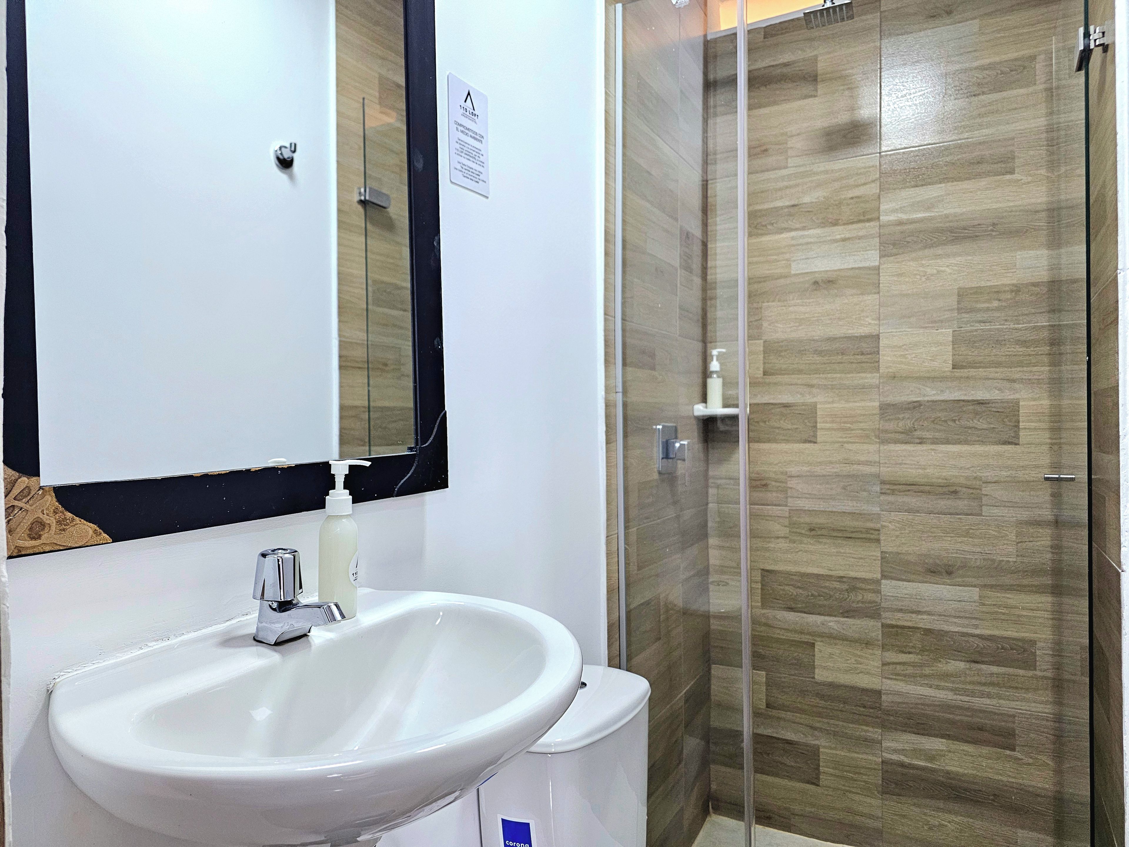 A bathroom with a white sink, a mirror, and a shower area with wooden flooring.