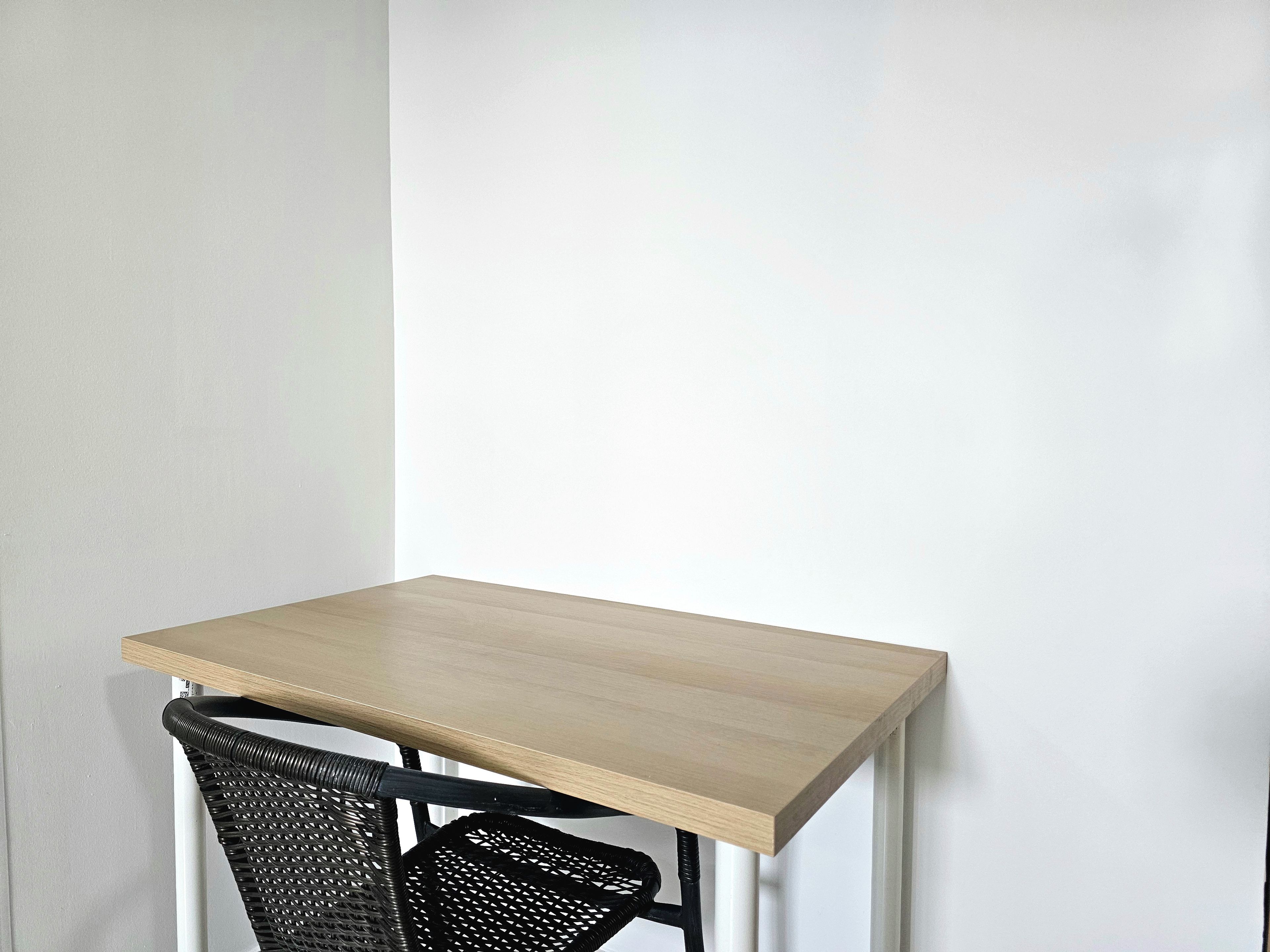 A small, square table with a light wood top and black metal legs, positioned against a white wall.