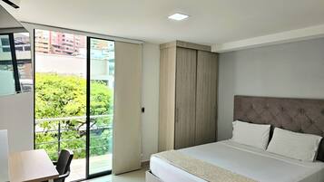 A hotel room with a bed, a desk, and a view of greenery and buildings through a large window.