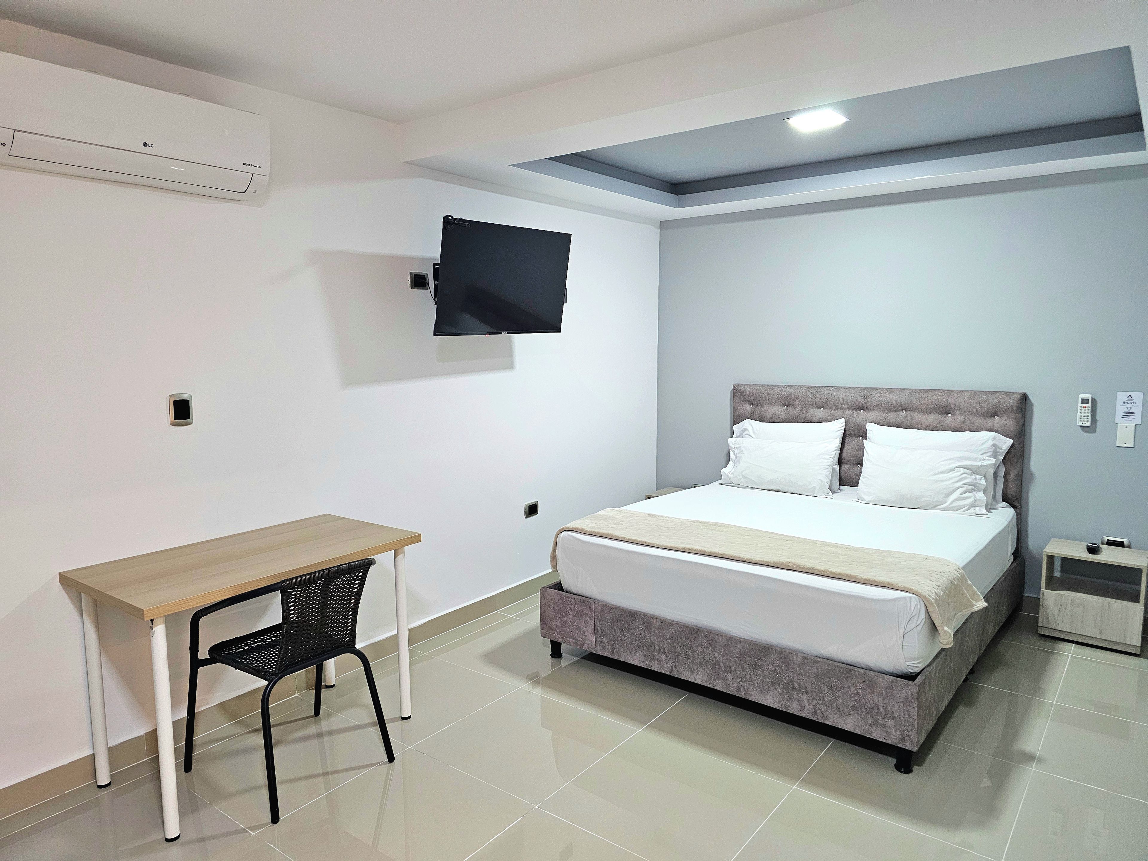 A bedroom with a bed, a desk, a chair, and a TV mounted on the wall.