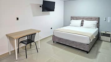 A bedroom with a bed, a desk, a chair, and a TV mounted on the wall.