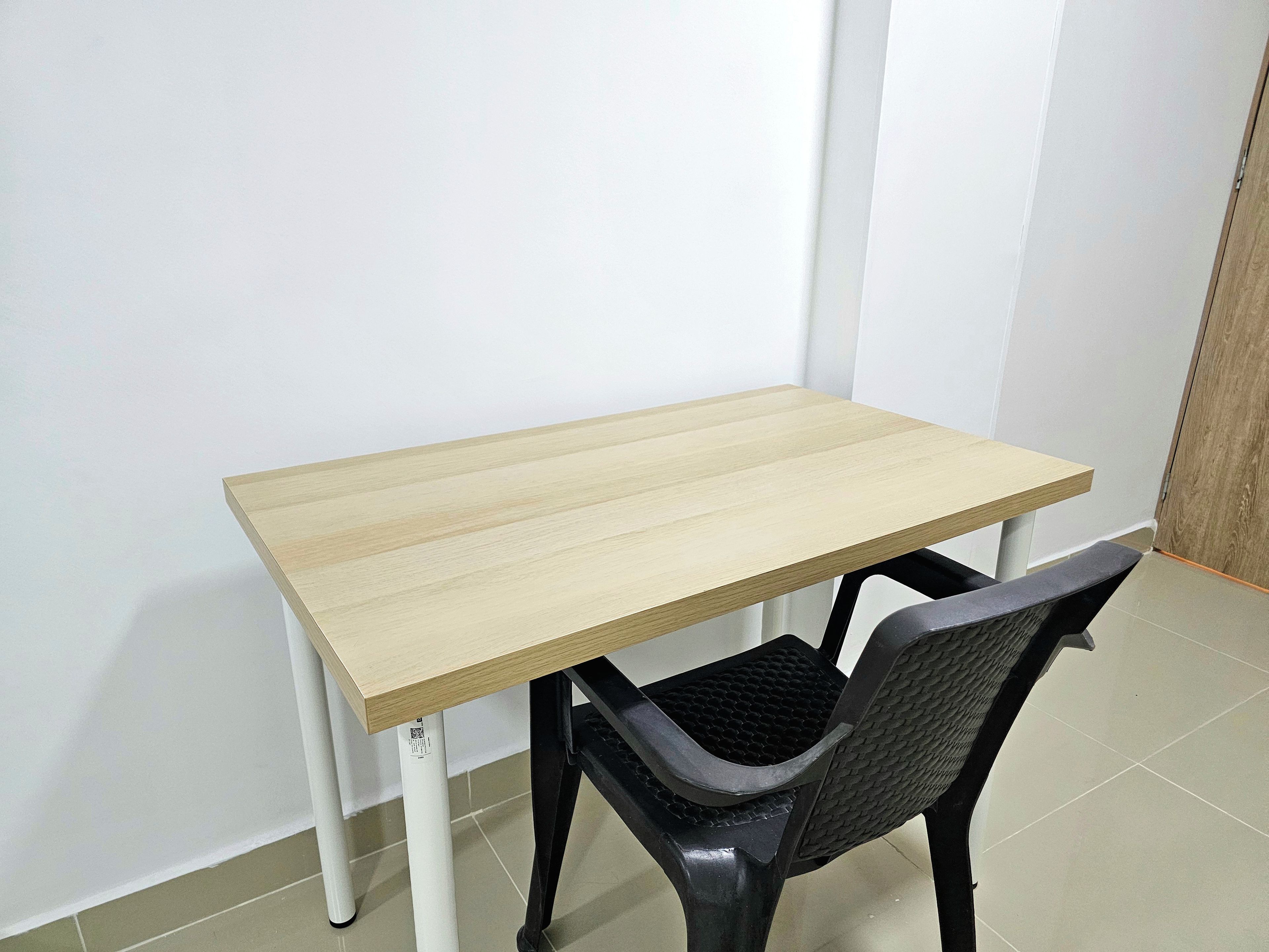 Een simpele tafel met een lichtgekleurd blad en zwarte poten, plus een zwarte stoel met een gestructureerde zitting.