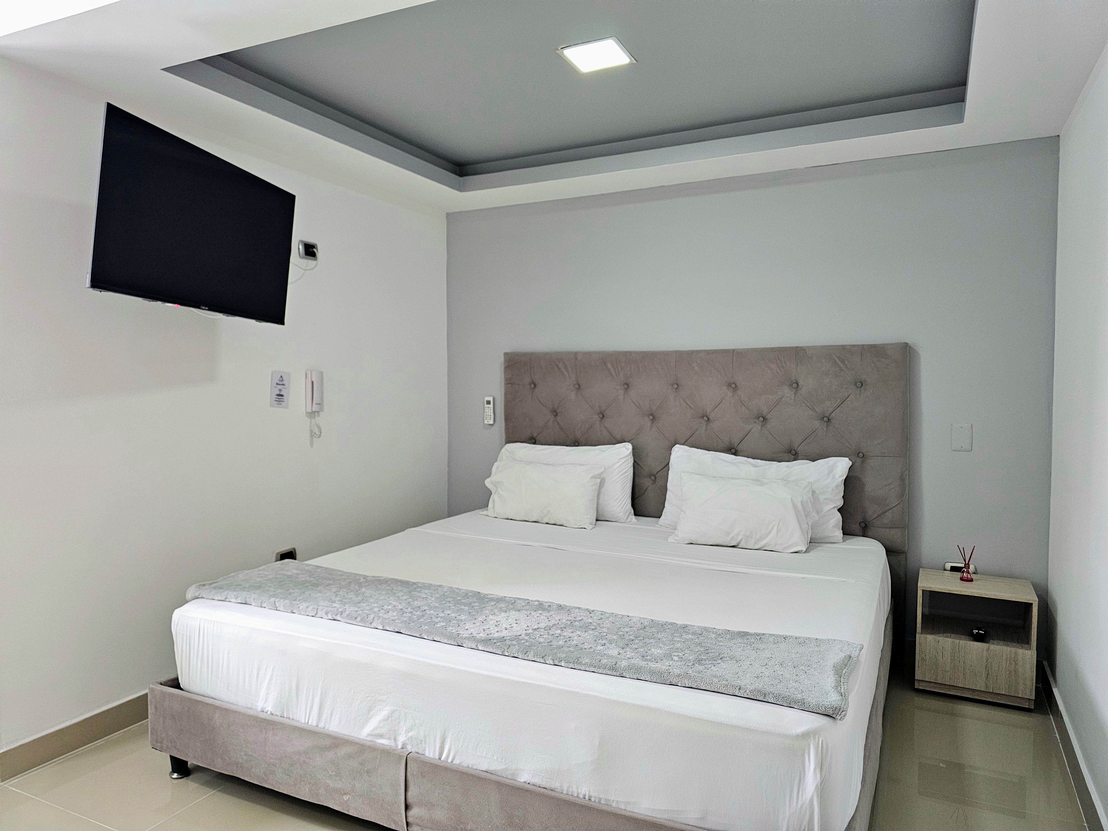 A modern bedroom with a large bed, a flat-screen TV mounted on the wall, and a bedside table with a lamp.