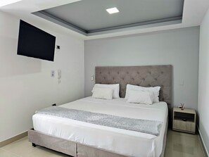 A modern bedroom with a large bed, a flat-screen TV mounted on the wall, and a bedside table with a lamp.