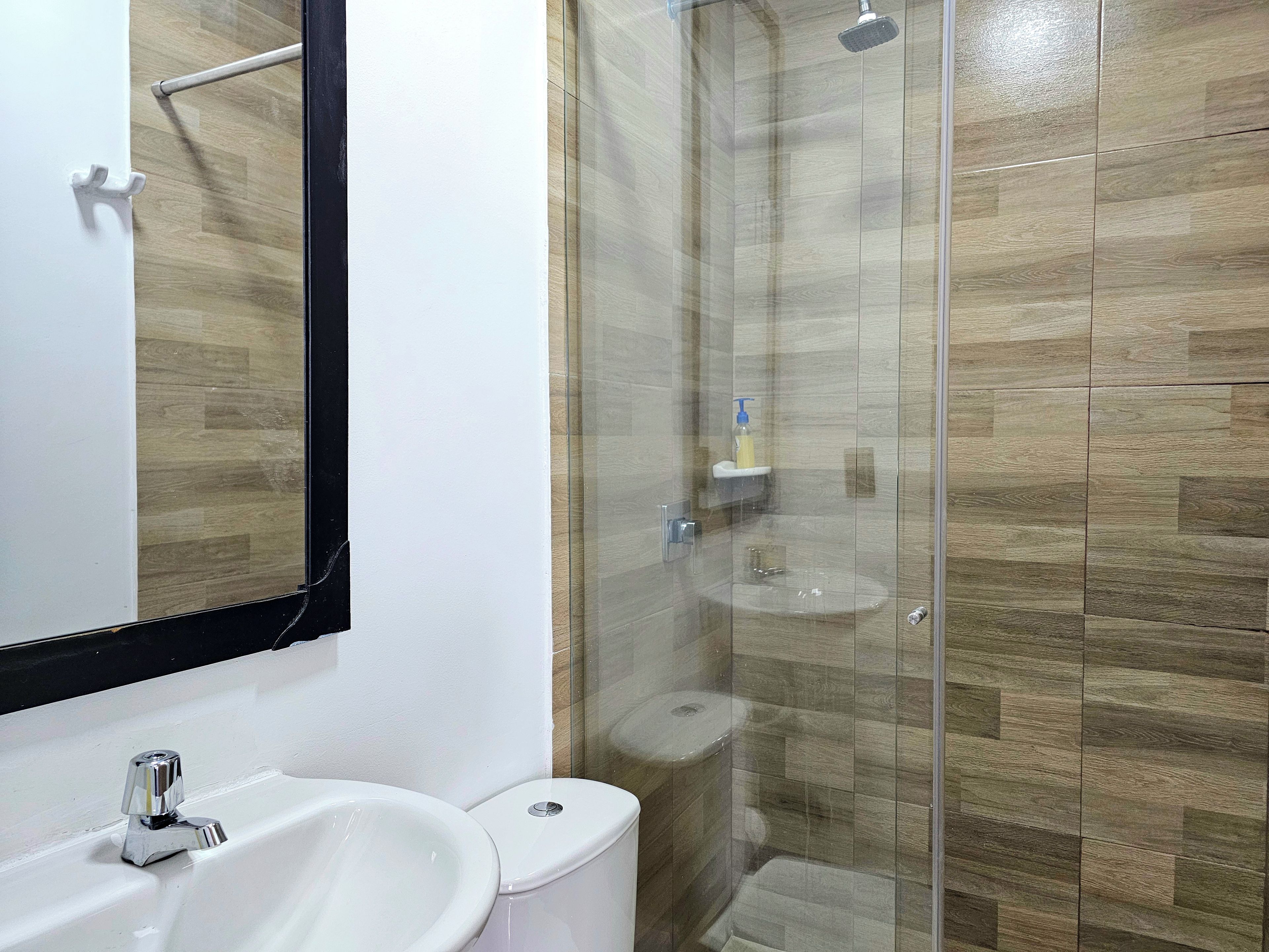 Un baño con un lavamanos blanco, un inodoro y una zona de ducha con mampara de vidrio.